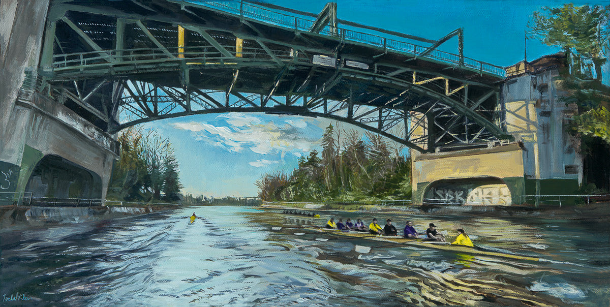 A framed print depicting a rowing team on water, with a bridge in the background under a clear sky.