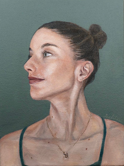 A realistic acrylic portrait painting of a women looking to her right. She wears her brunette hair in a high bun. The background is a blue-green, matching her eyes.